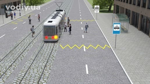 Трамвай на зупинці, дорожній знак 5.46.1 «Пункт зупинки трамвая», пішоходи виходять на проїзну частину для посадки у вагон.