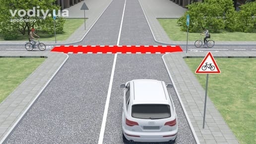 Дорожній знак 1.34 «Виїзд велосипедистів», білий автомобіль та велосипедисти на перетині велосипедної доріжки з дорогою поза перехрестям.