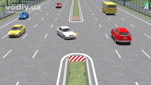 Білий автомобіль з увімкненим покажчиком повороту перед технологічним розривом розділювальної смуги на автомагістралі.