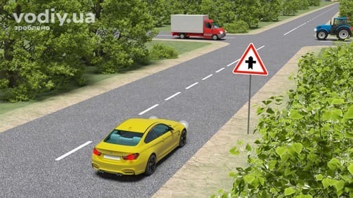 Жовтий автомобіль наближається до перехрестя, дорожній знак 1.22 «Перехрещення з другорядною дорогою», вантажівка та трактор на другорядній дорозі.
