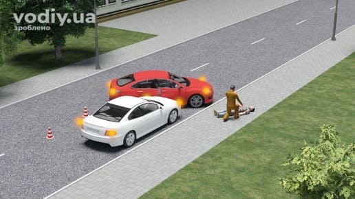 ДТП з потерпілим, водій надає допомогу людині на дорозі, два автомобілі з увімкненою аварійною сигналізацією та конуси на проїзній частині.