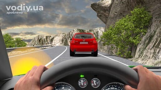 Червоний автомобіль попереду на гірській дорозі, крутий поворот праворуч з обмеженою оглядовістю, водій увімкнув лівий покажчик повороту.