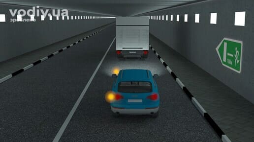 Легковий автомобіль з увімкненим лівим покажчиком повороту позаду вантажівки у тунелі, дорожній знак 5.80.1.