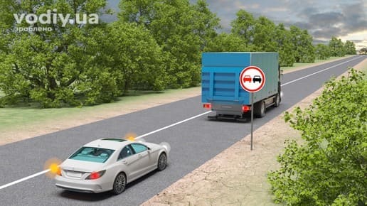 Дорожній знак 3.25 «Обгін заборонено», білий автомобіль з увімкненим покажчиком повороту та вантажівка на дорозі поза населеним пунктом.