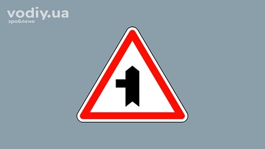 Дорожній знак 1.23.2 «Прилягання другорядної дороги» з лівого боку на сірому фоні.