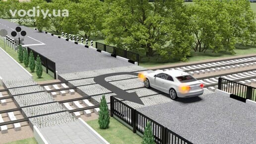 Білий автомобіль з увімкненим покажчиком повороту на залізничному переїзді, траєкторія розвороту на коліях.