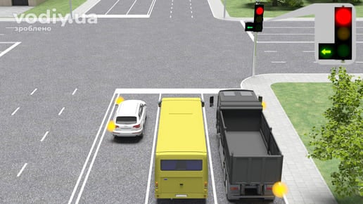 Білий автомобіль, автобус та вантажівка перед перехрестям, червоний сигнал світлофора та зелена стрілка у додатковій секції ліворуч.