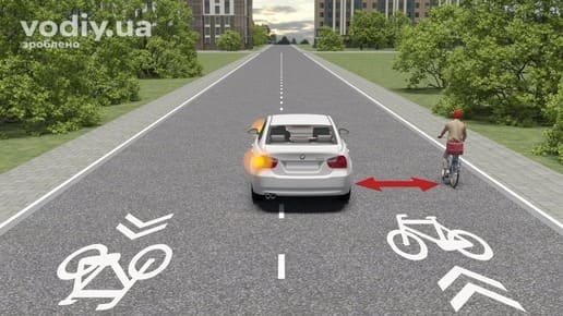 Білий автомобіль з увімкненим лівим покажчиком повороту та велосипедист на дорозі, безпечний бічний інтервал при обгоні велосипедиста.