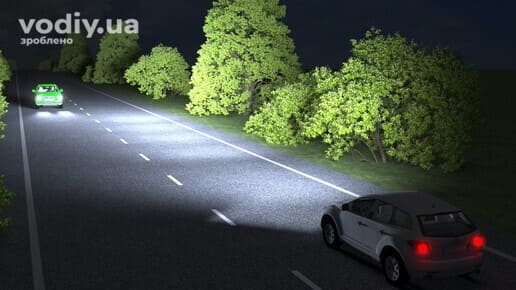 Білий та зелений автомобілі на нічній дорозі, увімкнене дальнє світло фар при наближенні зустрічного транспорту.