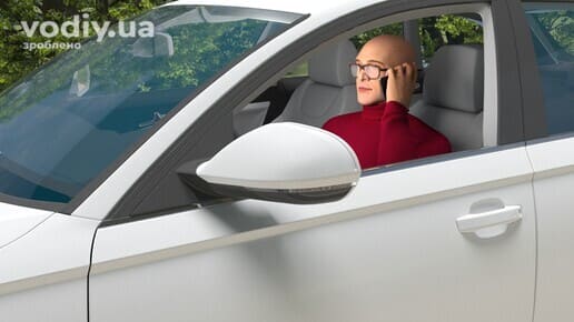 Водій за кермом автомобіля розмовляє по мобільному телефону, тримаючи його в руці під час руху.