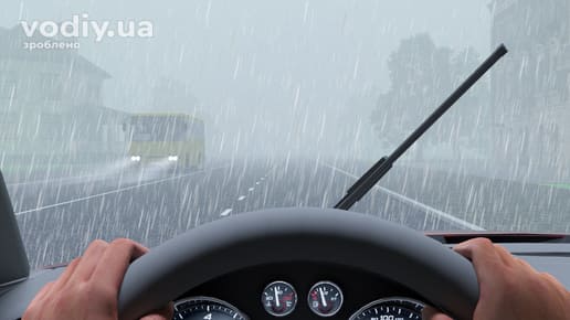 Вид з місця водія під час сильної зливи, робота склоочисників, обмежена видимість на дорозі та автобус попереду з увімкненими фарами.