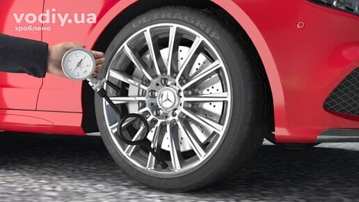 Перевірка тиску в шинах автомобіля за допомогою манометра, червоний кузов та легкосплавний диск.