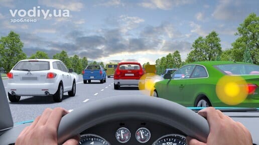 Зелений автомобіль з увімкненим лівим покажчиком повороту перестроюється у вашу смугу руху на багатосмуговій дорозі.