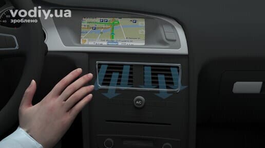 Рука водія біля дефлектора обдуву, кнопка кондиціонера A/C на центральній панелі та екран навігатора в салоні автомобіля.