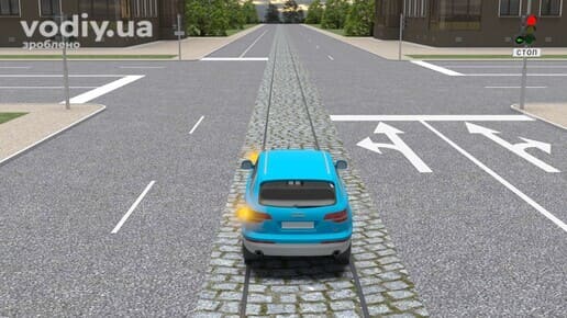 Автомобіль на трамвайній колії перед перехрестям, горизонтальна дорожня розмітка 1.18, червоний сигнал світлофора та табличка 5.69.