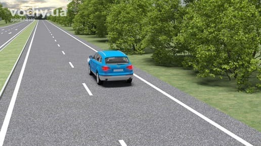 Синій легковий автомобіль на дорозі з розділювальною смугою поза населеним пунктом, край проїзної частини та зелені насадження.