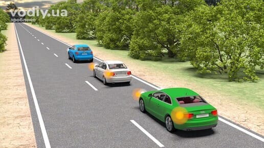 Зелений та білий автомобілі з увімкненими лівими покажчиками повороту на дорозі поза населеним пунктом, початок обгону декількох транспортних засобів.