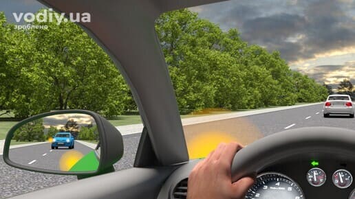 Вигляд з салону автомобіля, у дзеркалі заднього виду синій автомобіль з увімкненим лівим покажчиком повороту розпочав обгін.