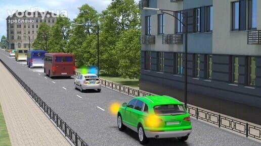 Зелений автомобіль з увімкненим покажчиком повороту позаду колони та поліцейського авто з синім і зеленим проблисковими маячками.