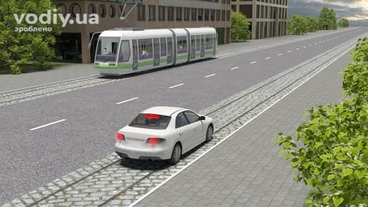 Білий автомобіль зупинився на трамвайній колії біля правого краю проїзної частини, трамвай на зустрічній колії.