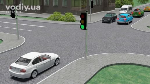 Білий автомобіль перед перехрестям, зелений сигнал світлофора та затор із транспортних засобів на виїзді з перехрестя.