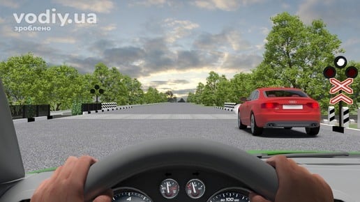 Червоний автомобіль перед залізничним переїздом, білий миготливий сигнал світлофора, рух через переїзд у два ряди.